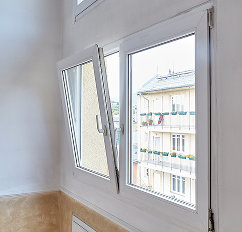 modern window opening with a view of an apartment building featuring twelve balconies showcasing vibrant flowers and laundry hanging